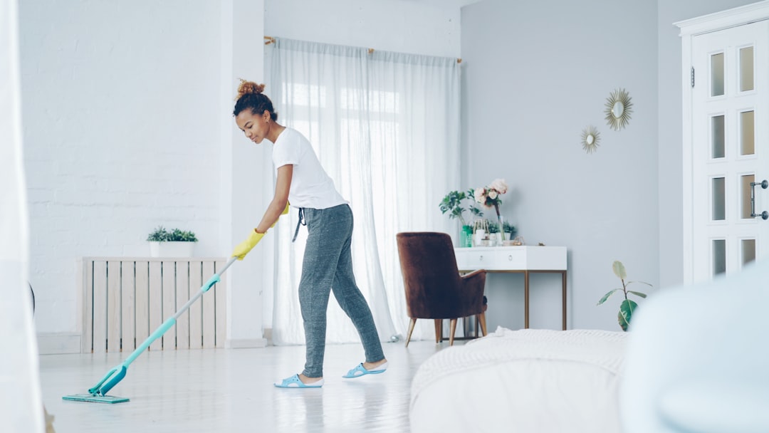 team-01 Pretty African American girl is mopping floor at home with flat plastic mop wearing gloves and wear-at-home clothing. Modern interiors, cleanness and young people concept.